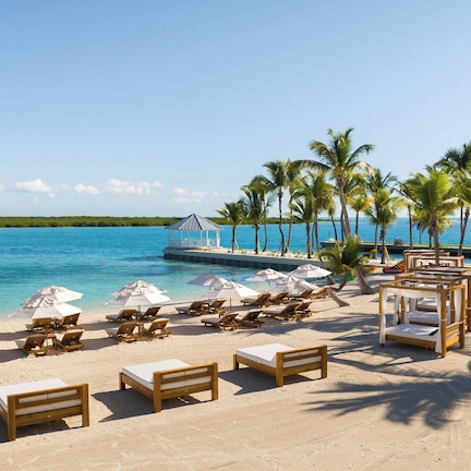 A beach with lounge chairs, umbrellas, and a wooden structure by the water.