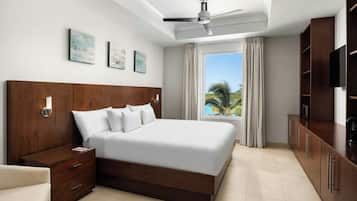 Une chambre d’hôtel moderne avec un grand lit, une table de chevet, une télévision et une fenêtre donnant sur des palmiers.