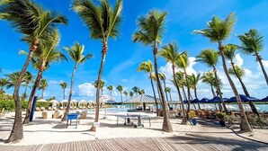Een strandresort met palmbomen, een zwembad en buitenzitplaatsen.