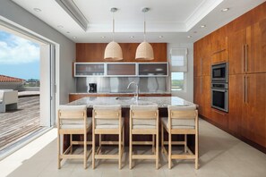 A modern kitchen with a central island, wooden cabinets, stainless steel appliances, and a large window overlooking a deck.