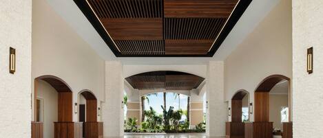 A spacious lobby with a high ceiling, wooden panel accents, and a view of palm trees.