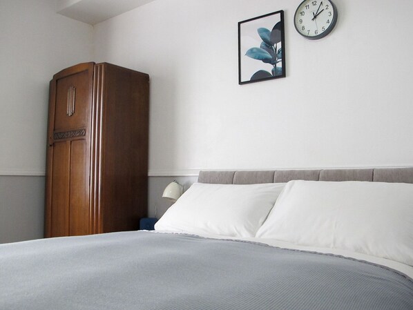 A bedroom with a bed, a wooden wardrobe, a wall clock, and a framed picture. - Stone's Throw Guesthouse (Weymouth)