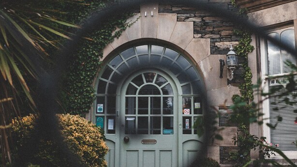 Un edificio con fachada de piedra, una puerta verde y un ventanal circular. Se identifica con el rótulo 