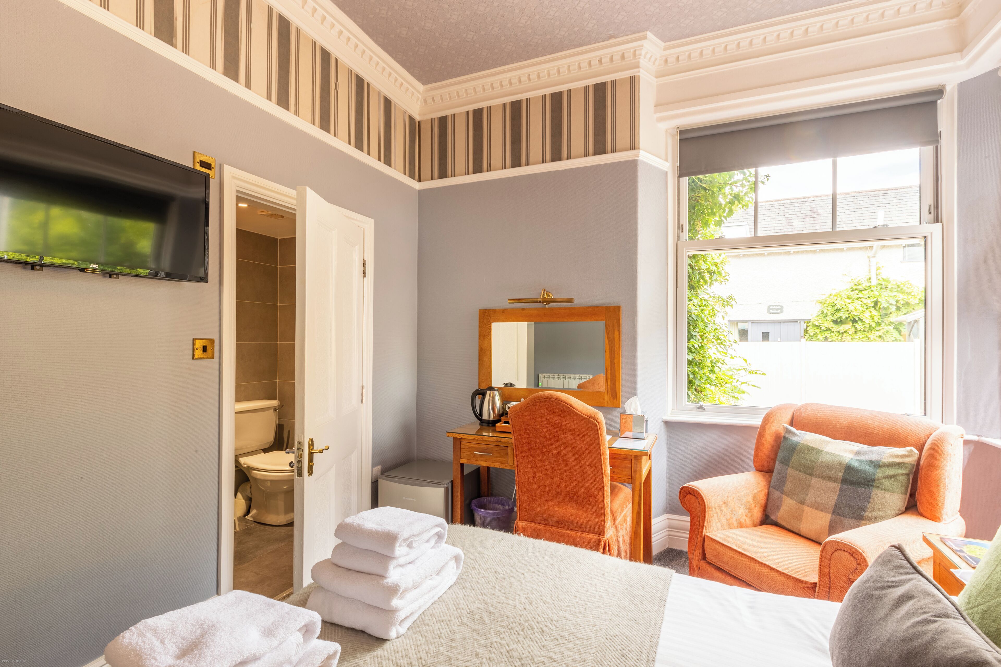 Ein Hotelzimmer mit Bett, Schreibtisch, Stuhl, Fernseher und Fenster.