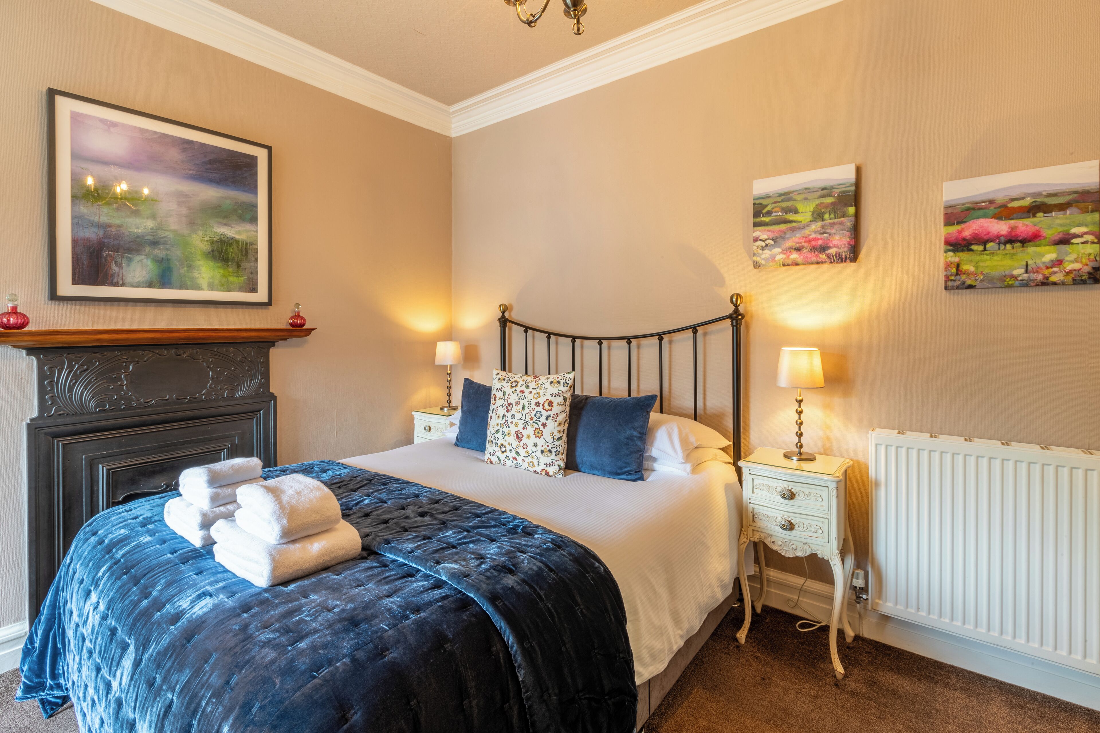 A neatly made bed with a dark blue quilt, two pillows, and a bedside table with a lamp.