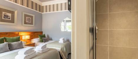 A hotel room with two beds, a chandelier, framed pictures on the wall, and a shower area.