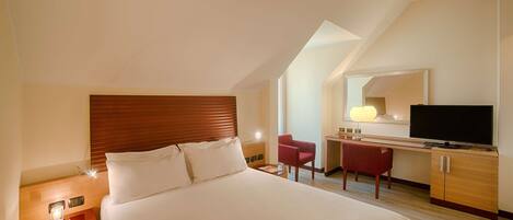 Una habitación de hotel con una cama grande, un escritorio con silla, un televisor y un espejo.