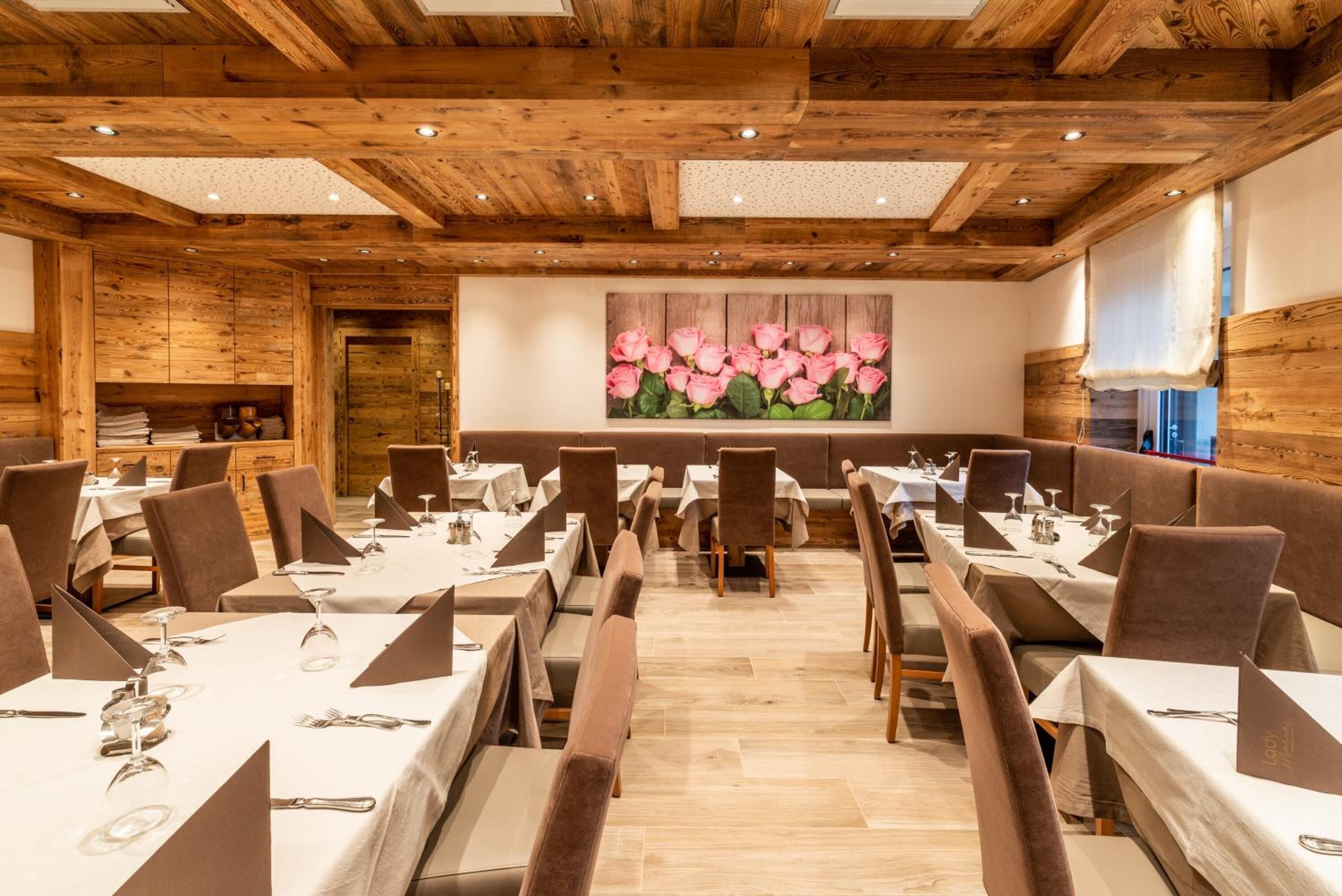 A restaurant with wooden ceiling beams, tables set for dining, and a large floral mural on the wall.