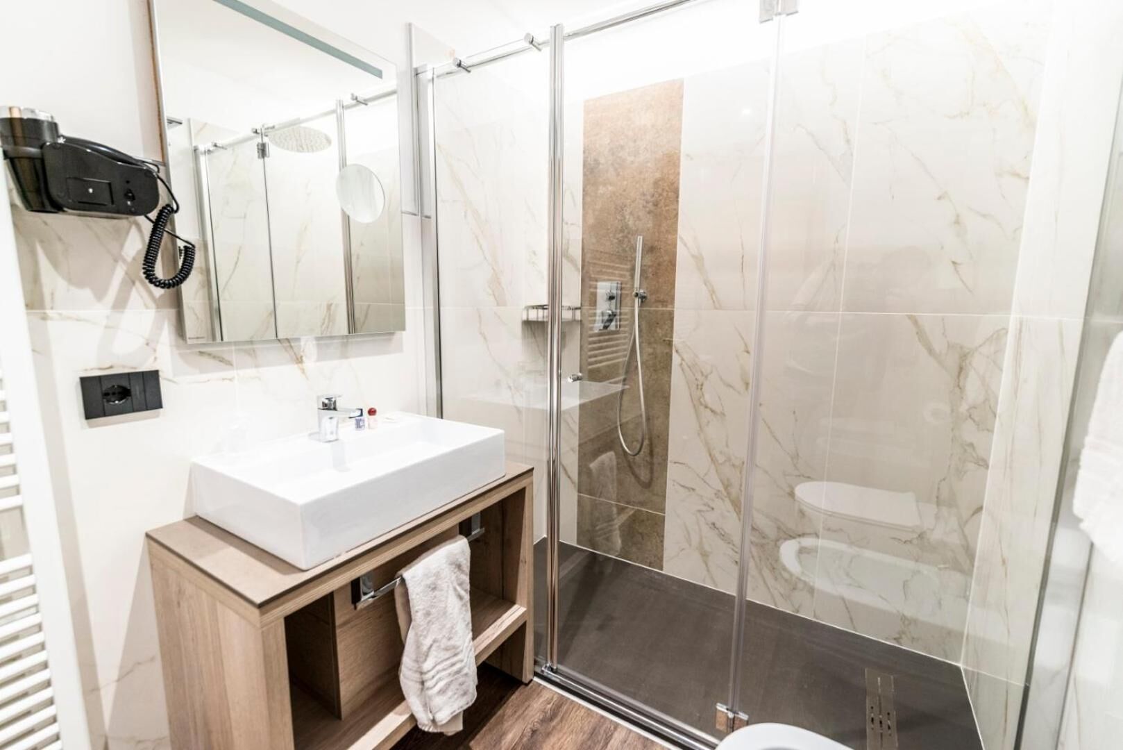 A modern bathroom with a glass-enclosed shower, a white sink, and a hairdryer mounted on the wall.