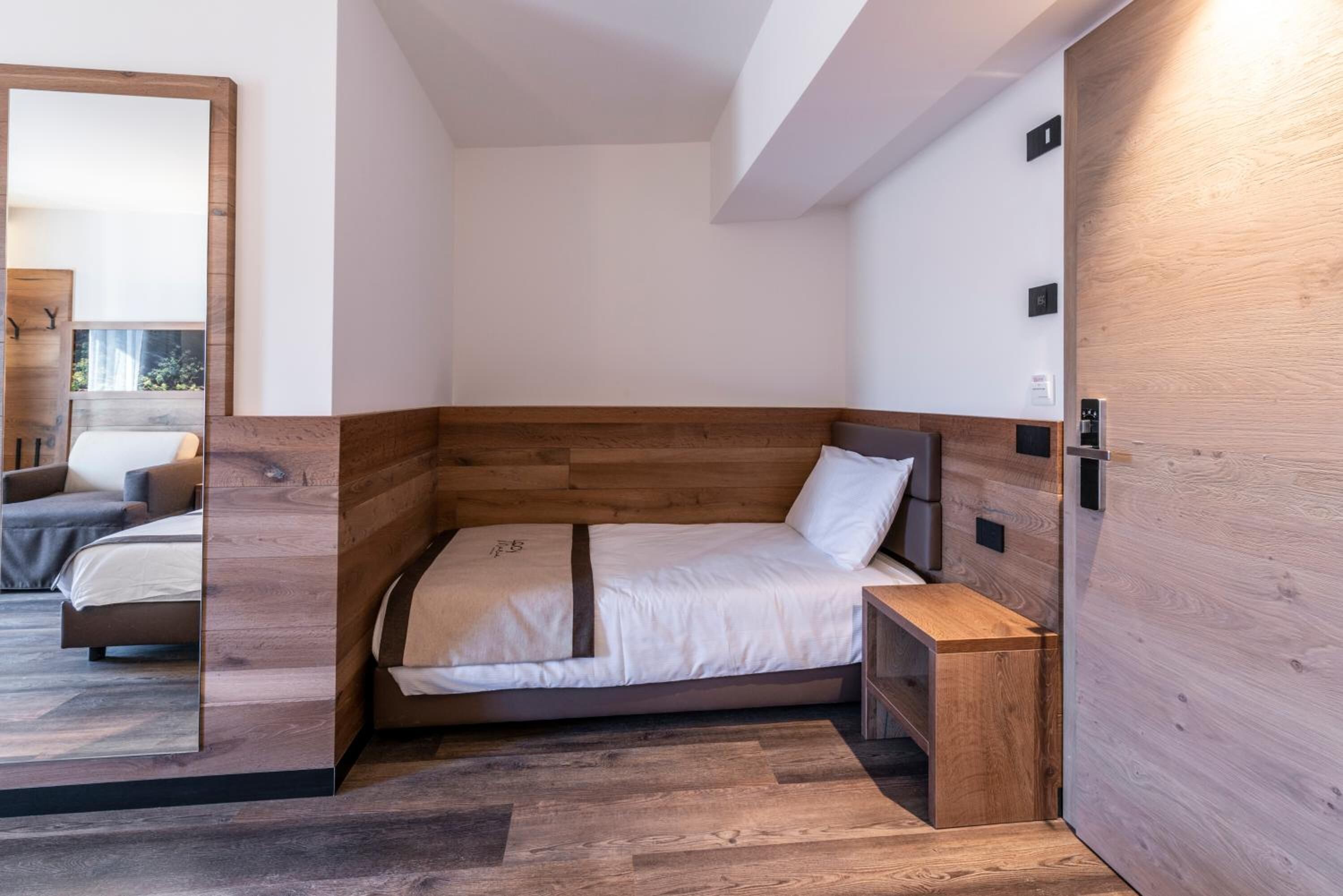 A modern bedroom with a wooden headboard, a single bed, a bedside table, and a mirror.