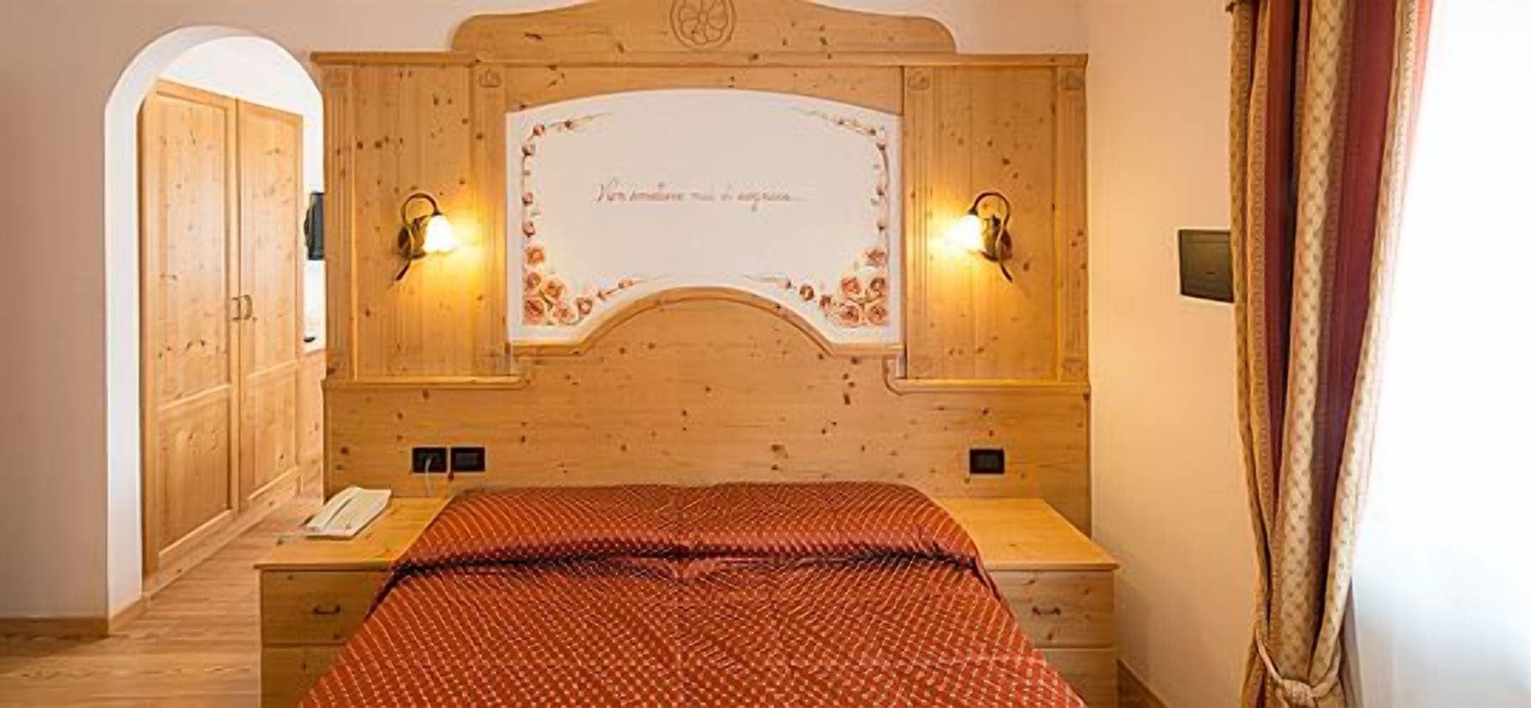 A wooden-paneled bedroom with a bed, two wall-mounted lamps, and a mirror.