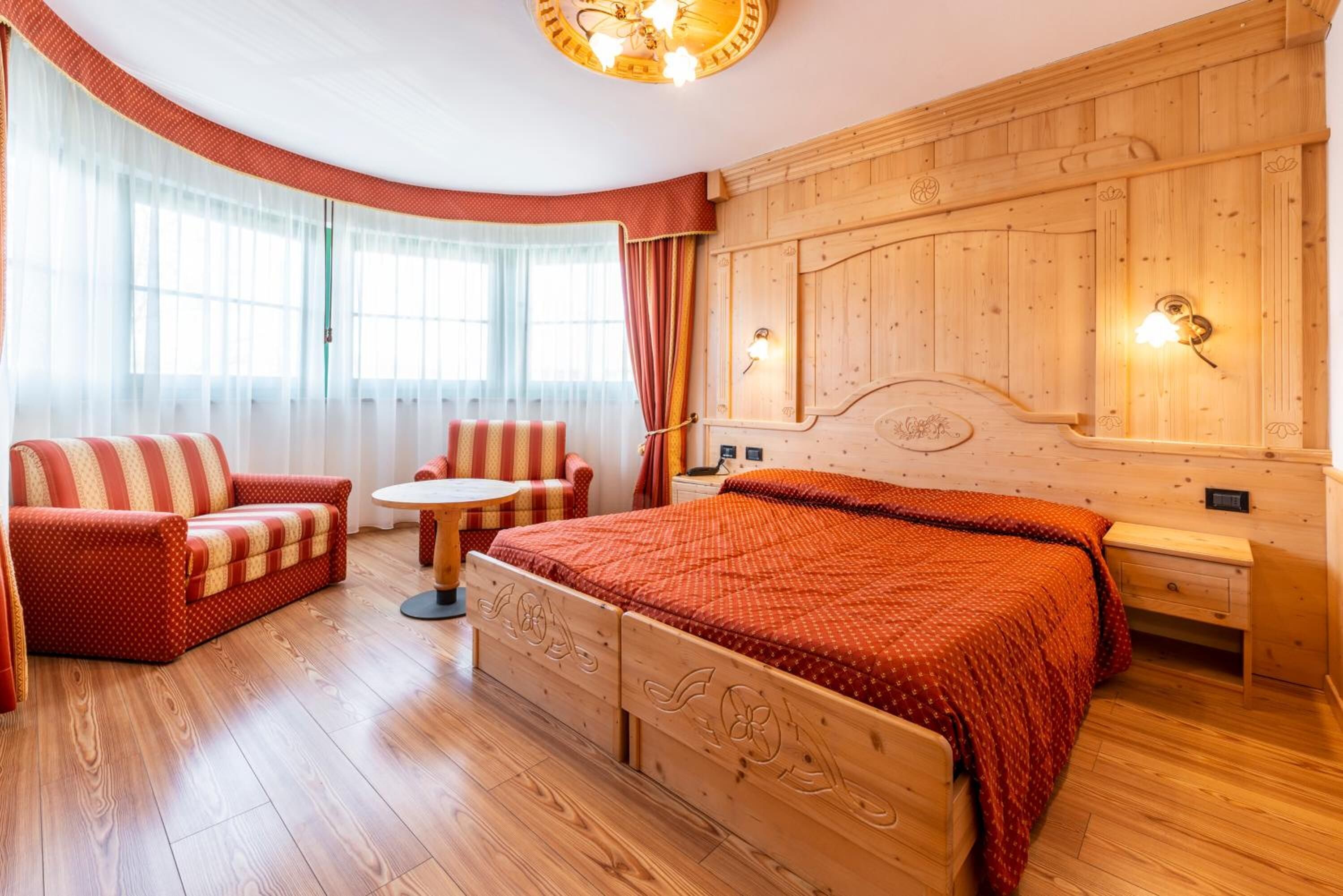 Ein gemütliches Zimmer mit einem hölzernen Bett, einem roten Sofa, einem kleinen runden Tisch und einem Stuhl.