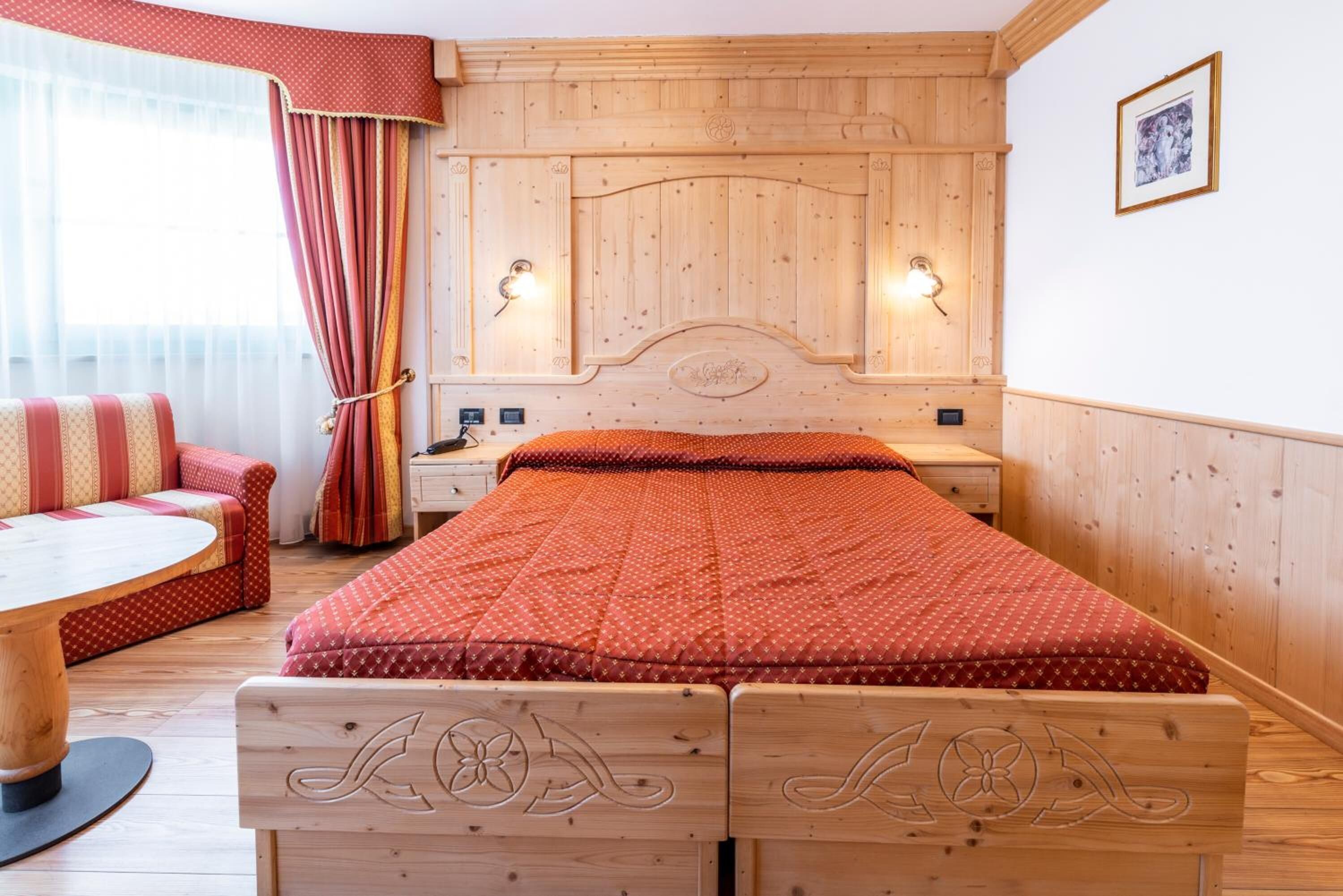A wooden bed with a red quilt, a wooden nightstand, a wooden chair, and a wooden table.
