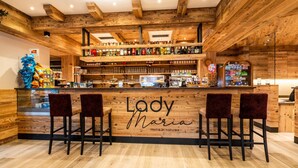 Een bar met houten inrichting, barstoelen en een toonbank met verschillende flessen en snacks.