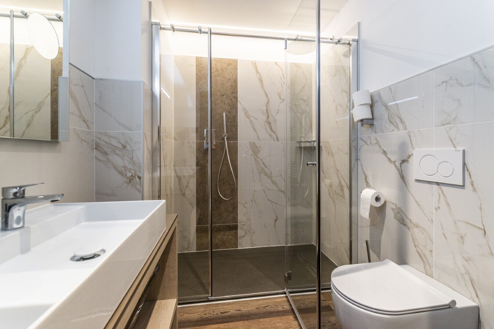 Un bagno moderno con box doccia in vetro, lavandino bianco e water.
