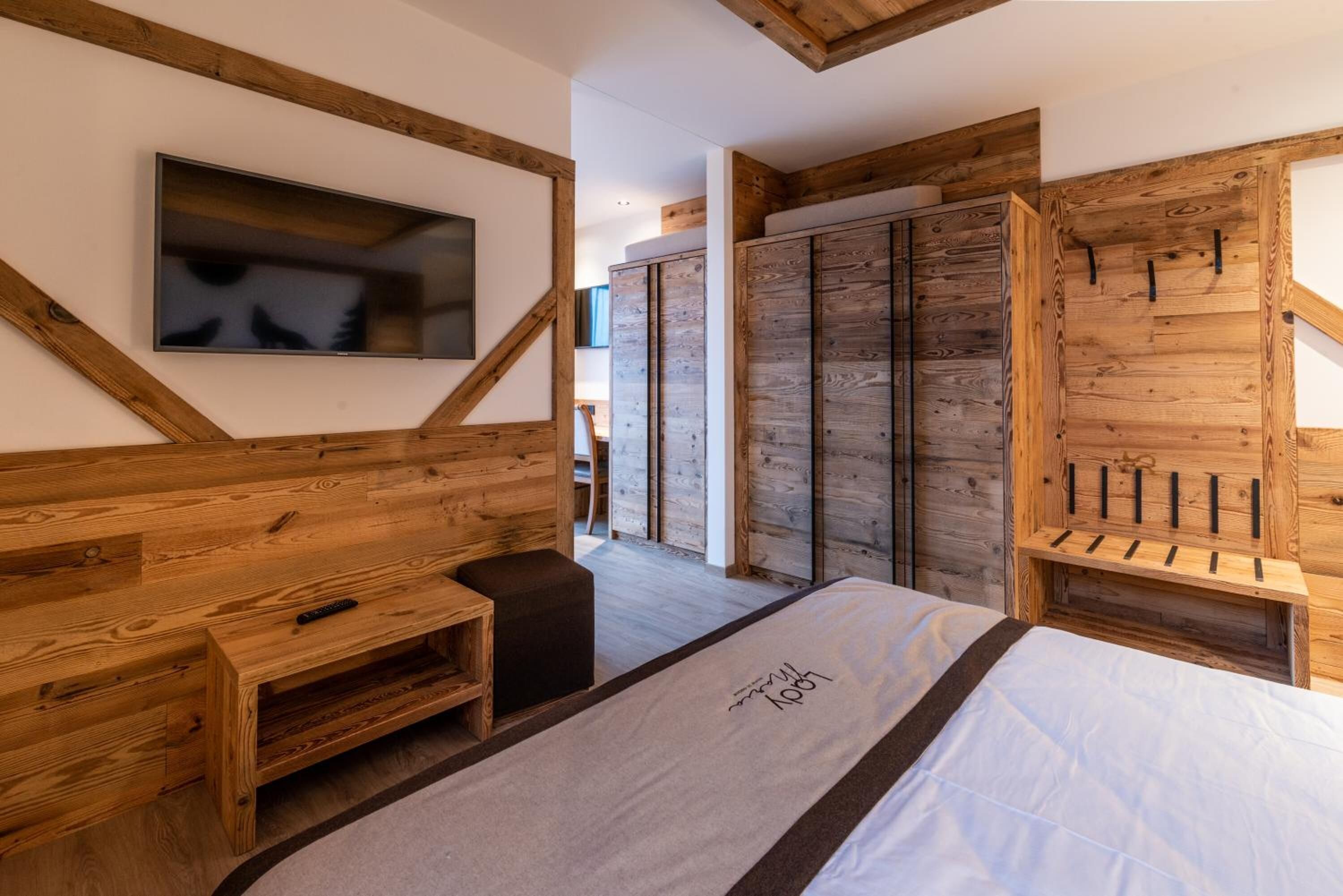 Un dormitorio con cama, cabecera de madera, televisor montado en la pared y un armario de diseño rústico.