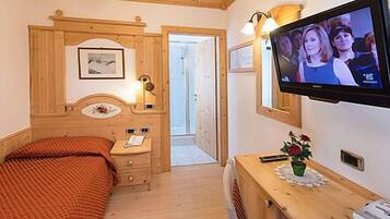 Un dormitorio con cama, mesita de noche, lámpara, televisor y una pequeña mesa con un florero.