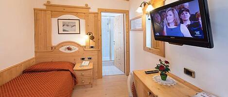 A bedroom with a bed, bedside table, lamp, TV, and a small table with a vase.