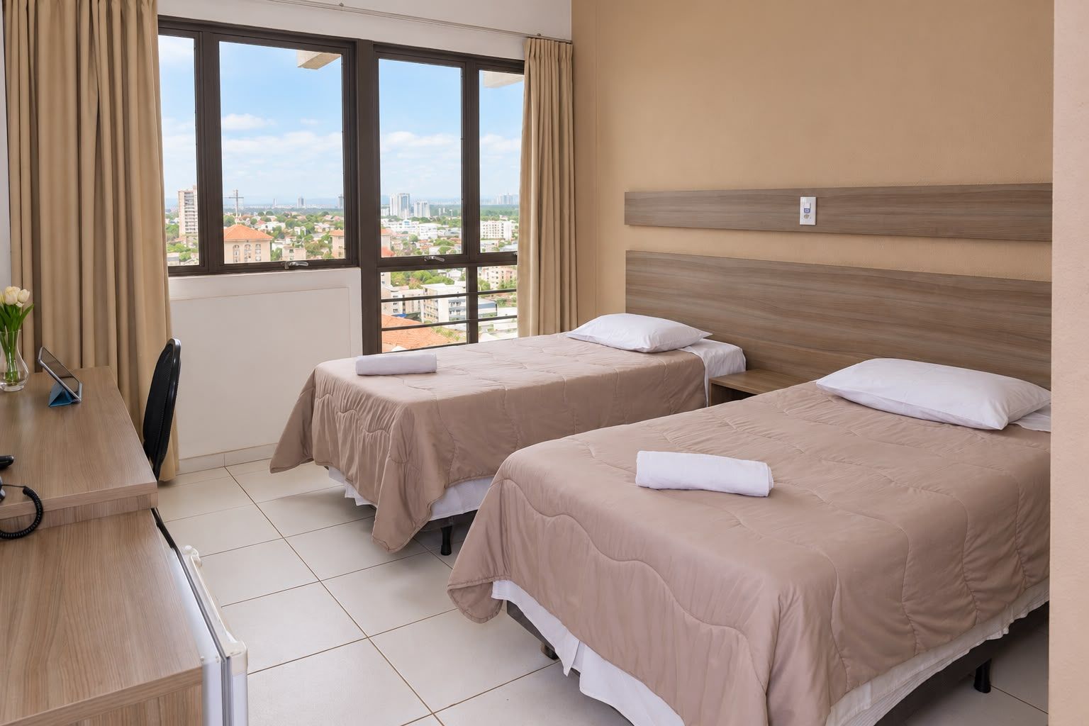 A hotel room with two beds, a desk, and a view of the city.