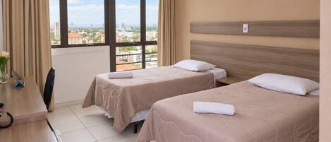 A hotel room with two beds, a desk, and a view of the city.