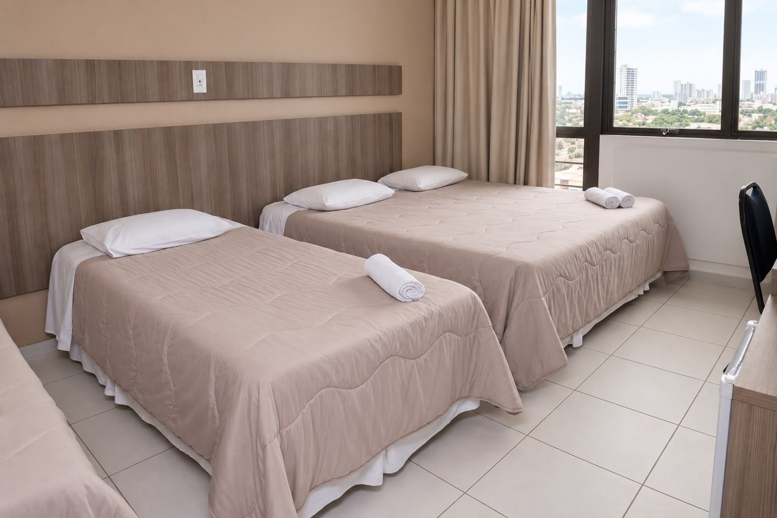 Habitación de hotel con dos camas, un escritorio y ventana con vista a la ciudad.