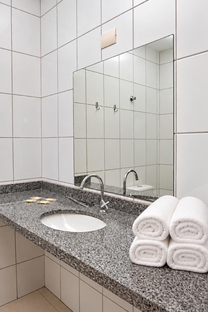 A bathroom with a granite countertop sink, a mirror, and a towel rack with towels.