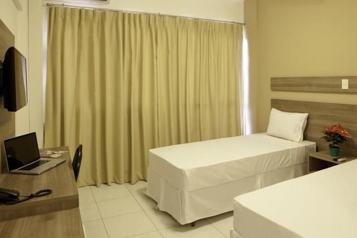 A hotel room with two beds, a desk with a laptop, a TV, and a curtain.