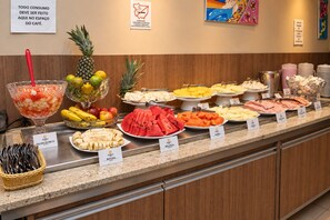 Un bufé con diversas frutas y platos, cada uno identificado con su nombre.