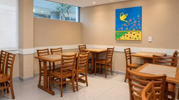 Un comedor con mesas y sillas de madera, un ventanal grande y una llamativa obra de arte en la pared.