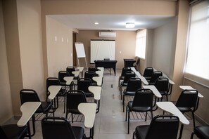 A conference room with rows of black and white chairs, a whiteboard, and an air conditioning unit on the wall. - Getúllio Hotel (Cuiabá)