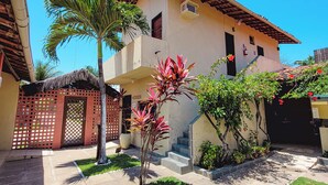 A two-story building with a tiled roof, a small porch, and a red gate. - Pousada Bore Koko (Ipojuca)