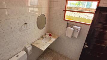 A small bathroom with a toilet, sink, and mirror. There is a window above the sink.