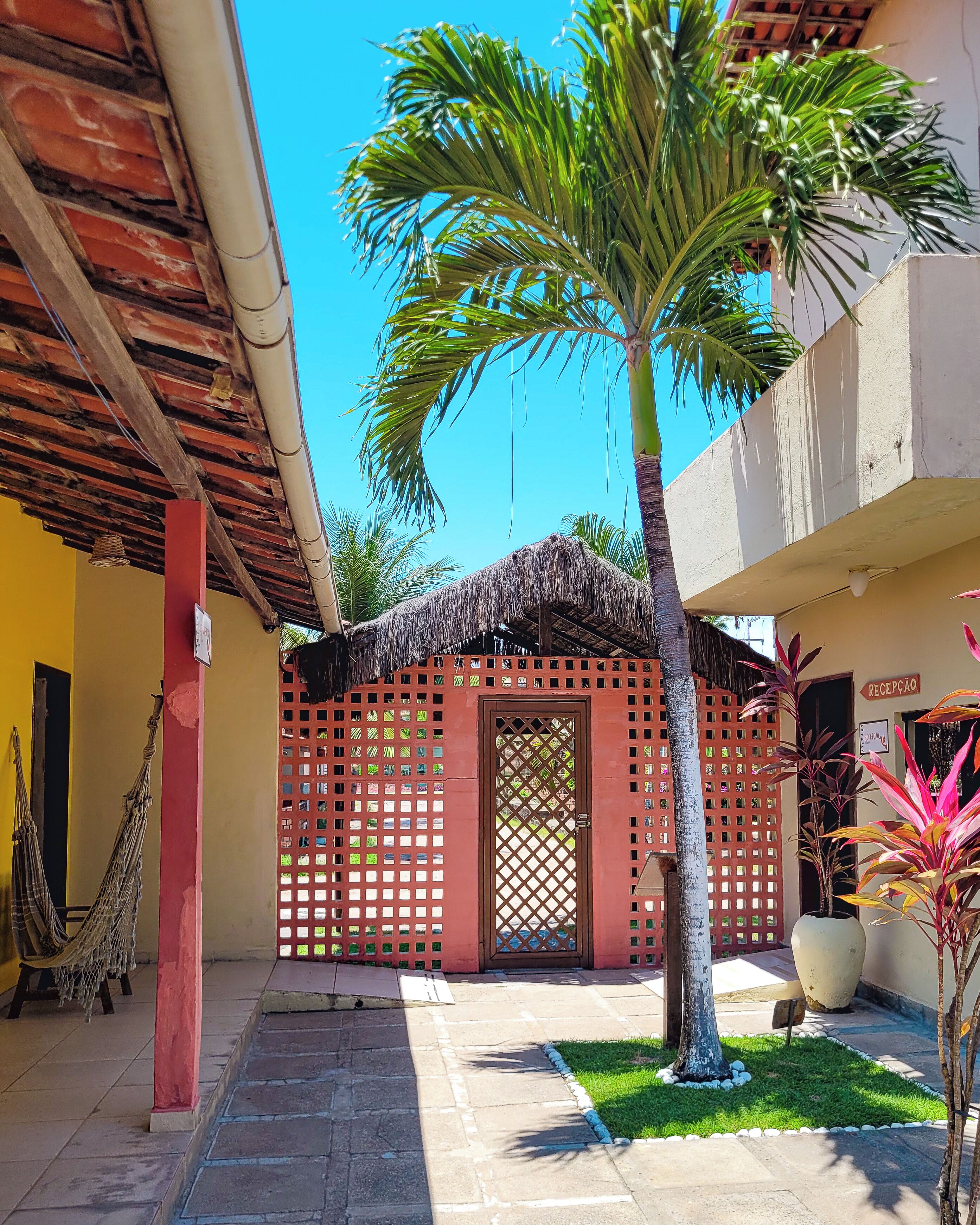 Un patio con una estructura de techo de paja, una palmera y un portón de celosía roja.