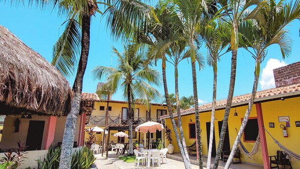 A courtyard with palm trees, outdoor seating, and a thatched-roof building. - Pousada Bore Koko (Ipojuca)