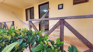 A yellow building with a wooden balcony railing, a hammock, and green plants. - Pousada Bore Koko (Ipojuca)