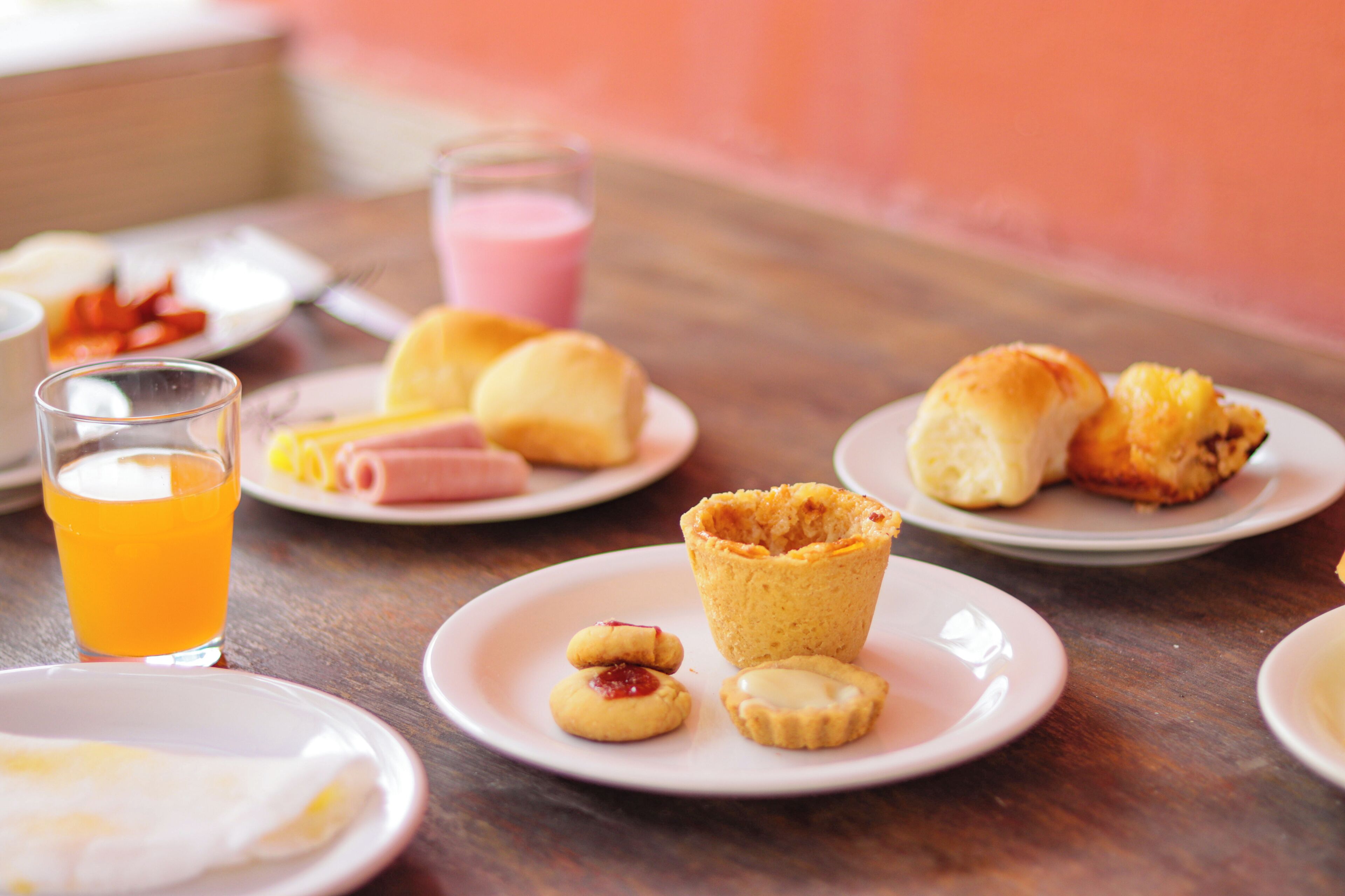 Uma mesa de café da manhã com diversos doces, um copo de suco de laranja e um prato de comida.
