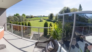 A balcony with a hot tub, wicker furniture, and a glass enclosure offering a view of a green landscape.