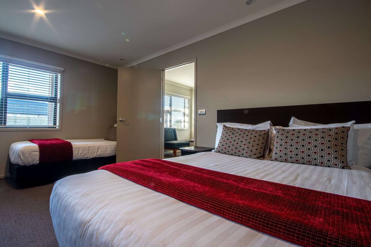 Une chambre d’hôtel avec un grand lit, un plus petit lit et une fenêtre avec des stores.