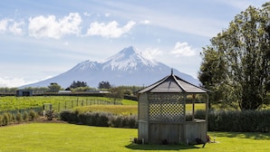 A wooden gazebo in a grassy field with a mountain in the background.