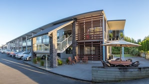 A modern building with a curved facade, outdoor seating area, and a parking lot.