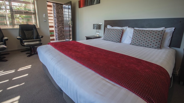 A hotel room with a large bed, a desk, a chair, a window with blinds, and a door.