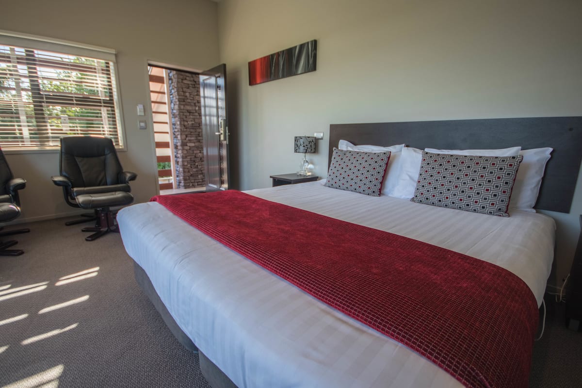 Une chambre d’hôtel avec un grand lit, un bureau, une chaise, une fenêtre avec des stores et une porte.