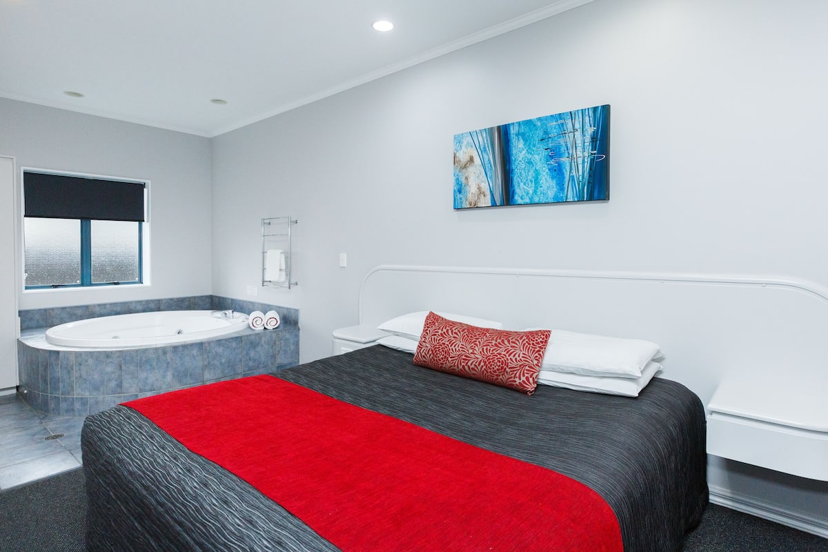A modern hotel room with a large bed, a separate bathroom with a bathtub, and a window with a view.