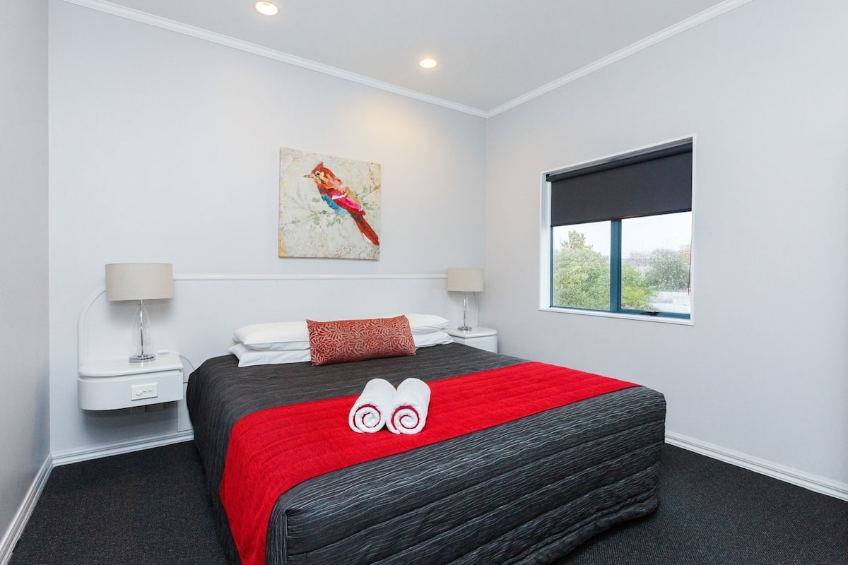 A hotel room with a bed, a window, a painting, and a lamp.