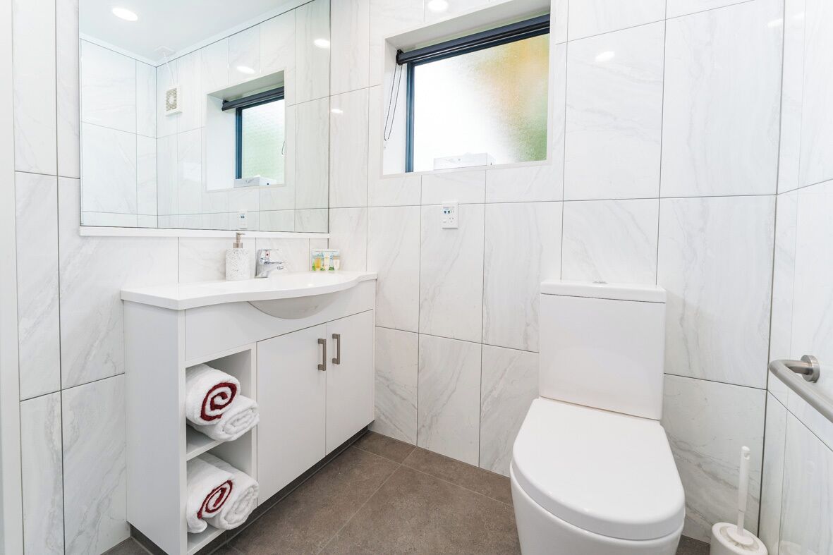 Un baño moderno con un lavabo de mármol blanco, un inodoro y un espejo sobre el lavabo.