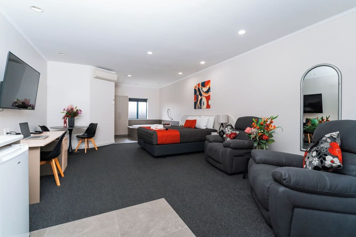 A modern living room with a sofa, a dining area with a table and chairs, a flat-screen TV mounted on the wall, and a large mirror.
