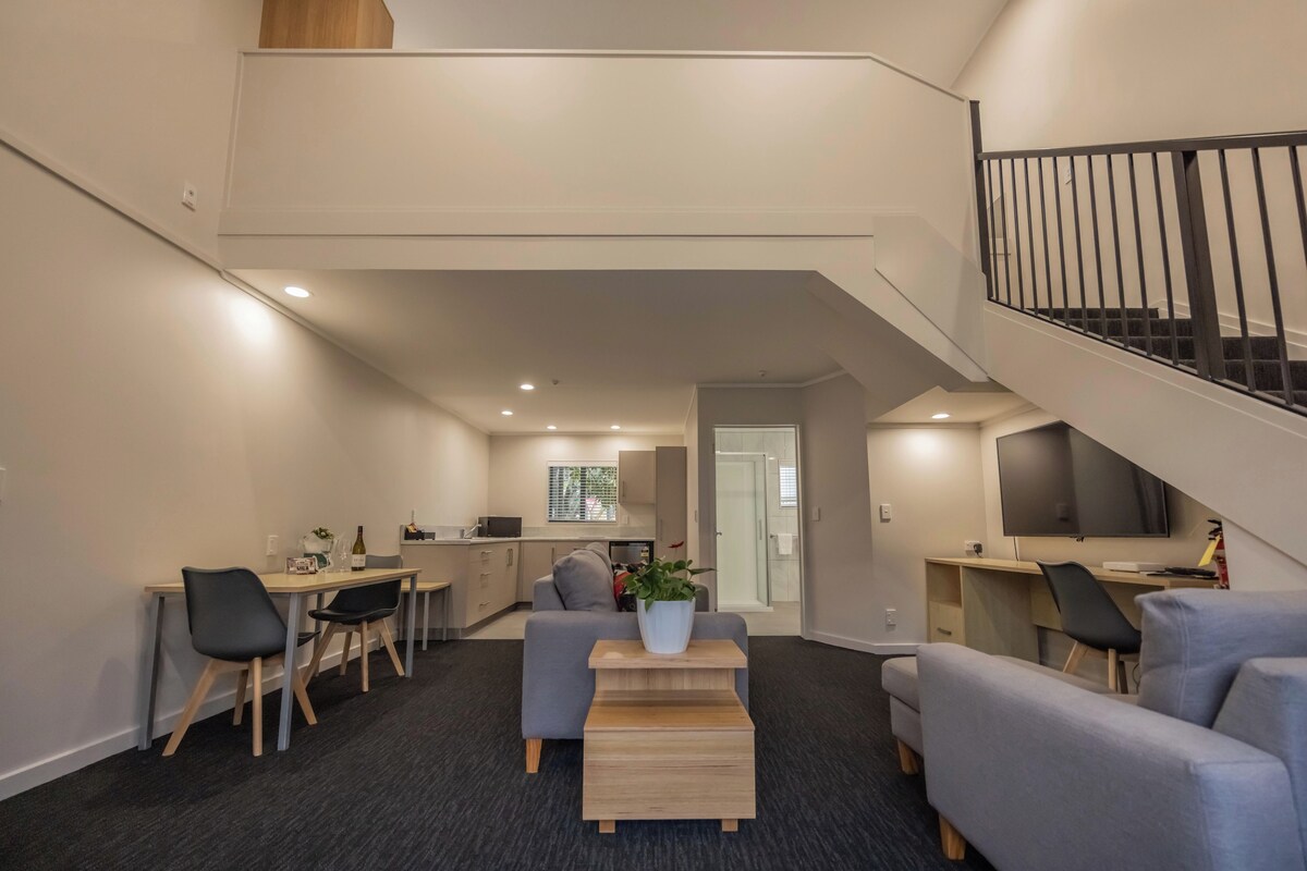 Un interior moderno con comedor, cocina y una escalera que sube a un nivel superior.
