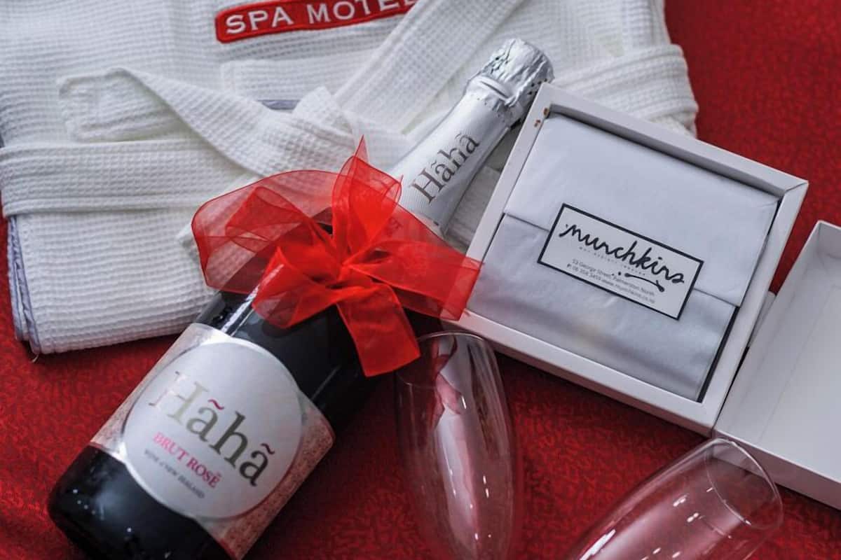 A bottle of 'Hahā' wine, two wine glasses, a white gift box with 'munchkins' branding, and a white towel with 'Aubyn Court SPA MOTEL' branding.