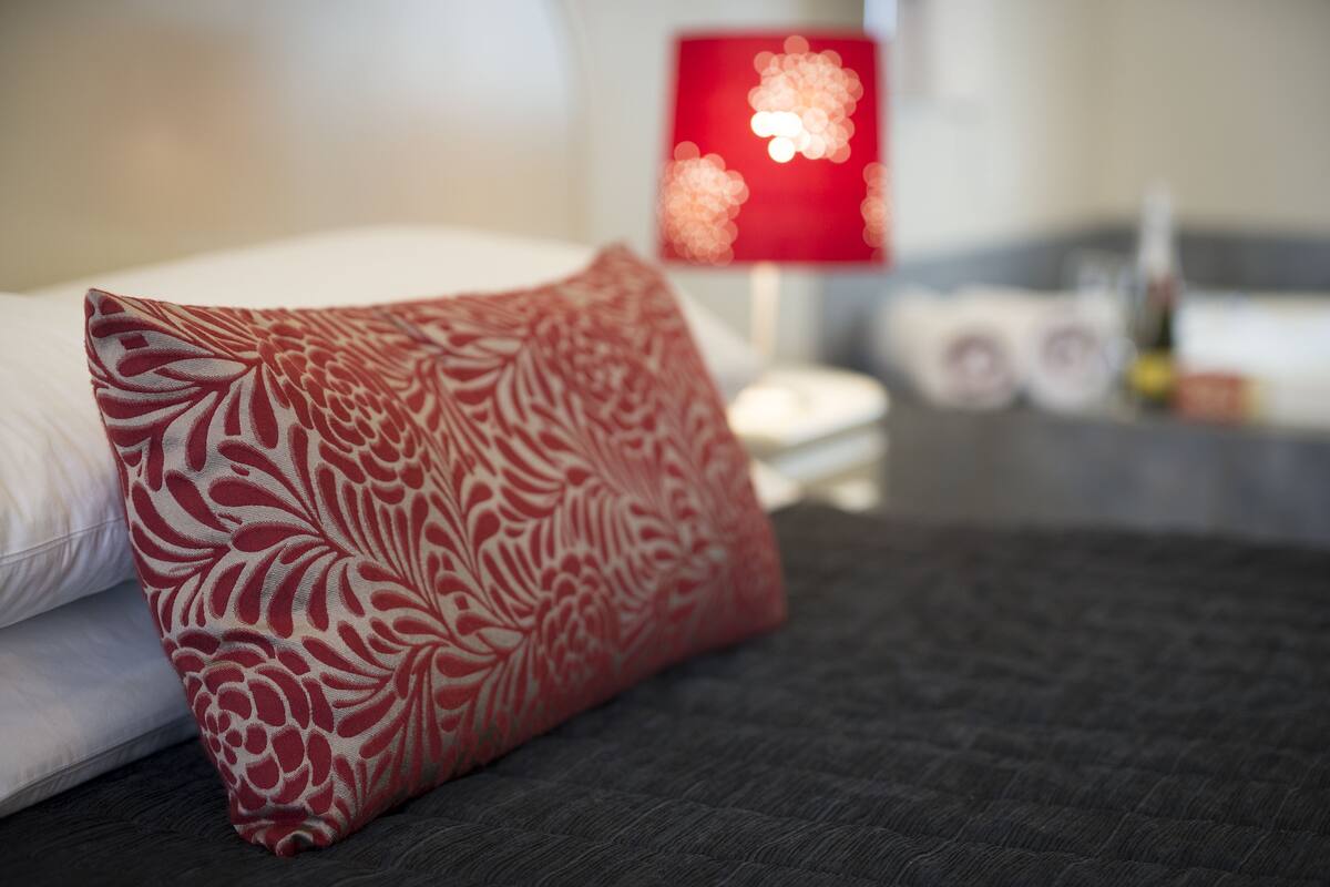A bed with a red patterned pillow, a white pillow, and a dark grey bedspread.
