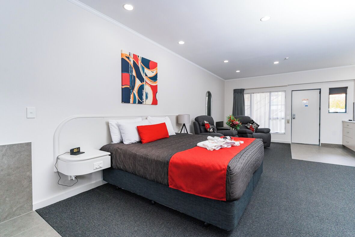 A modern hotel room with a large bed, a desk, a chair, and a small table.
